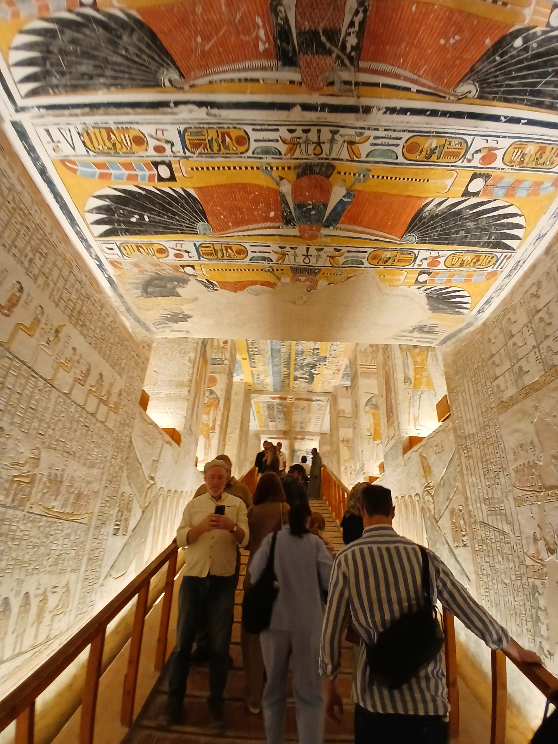 Tourists walking along a wooden path under a yellow-painted ceiling depicting the goddess Nut 