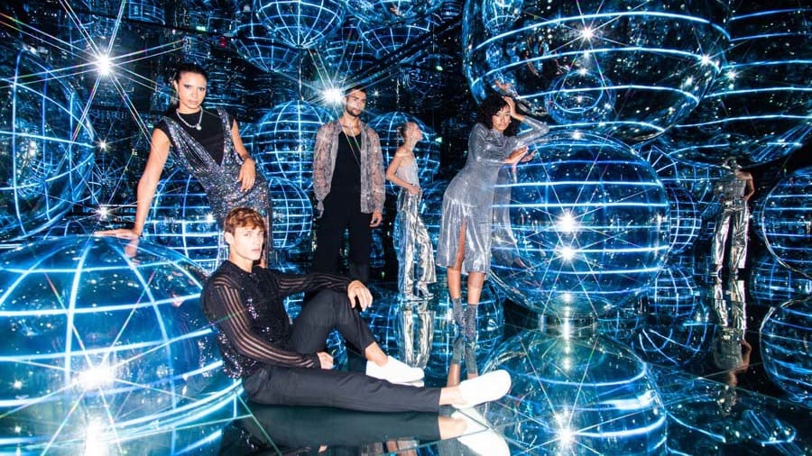 A group of visitors posing among large illuminated blue wireframe globes with bright star-like flares at AYA Universe Dubai