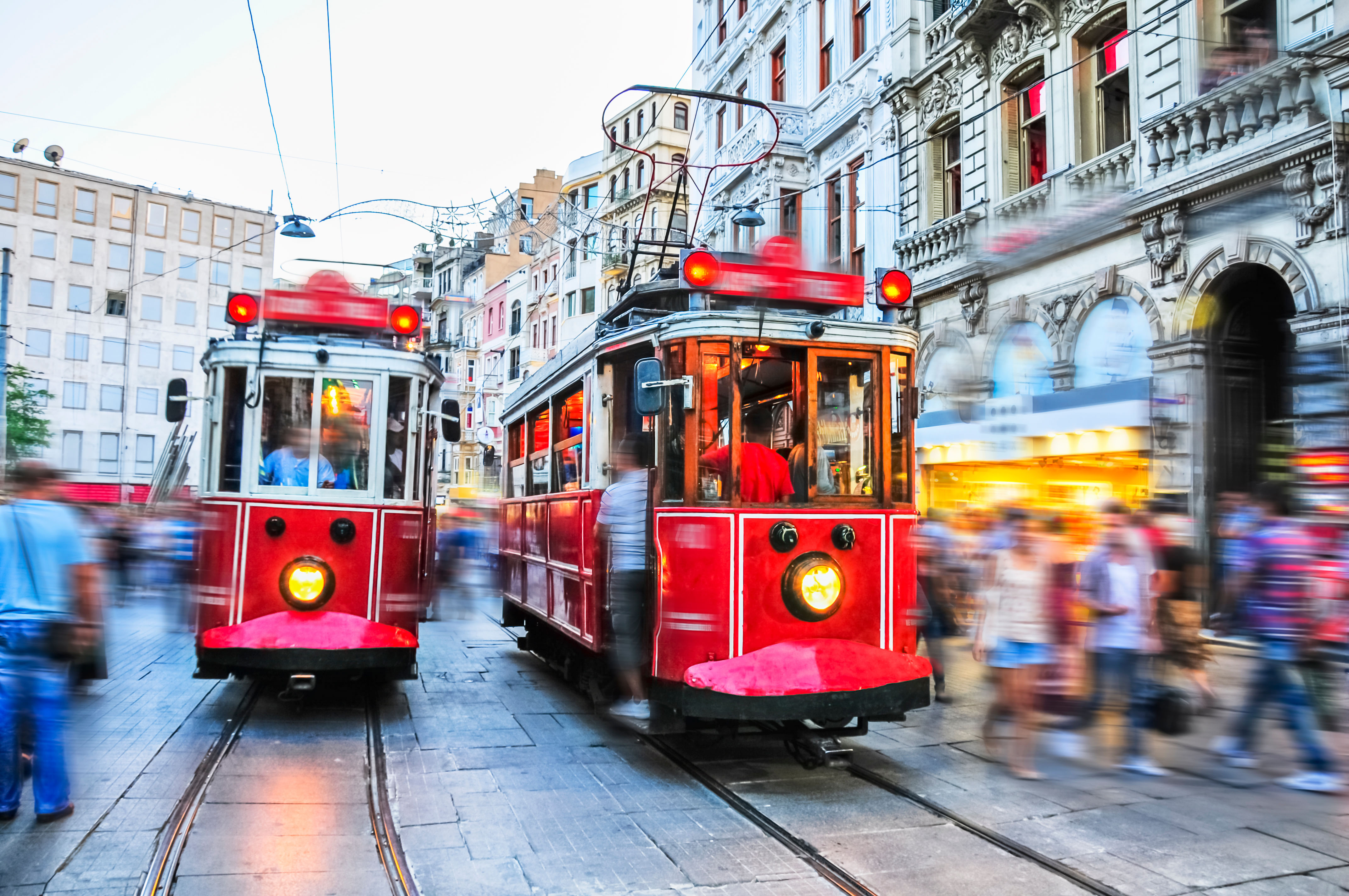 “Historic red tram traveling along crowded İstiklal Street in Taksim, Istanbul, with shops and pedestrians lining the street.”