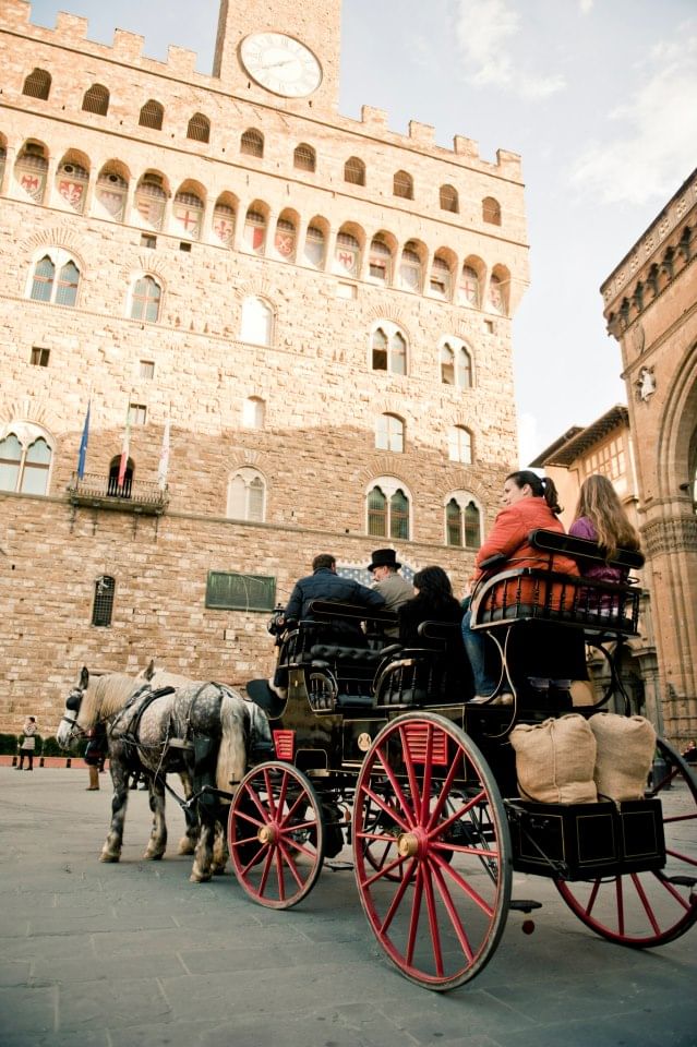 Rear view of a carriage with passengers on board in front of Palazzo Vecchio