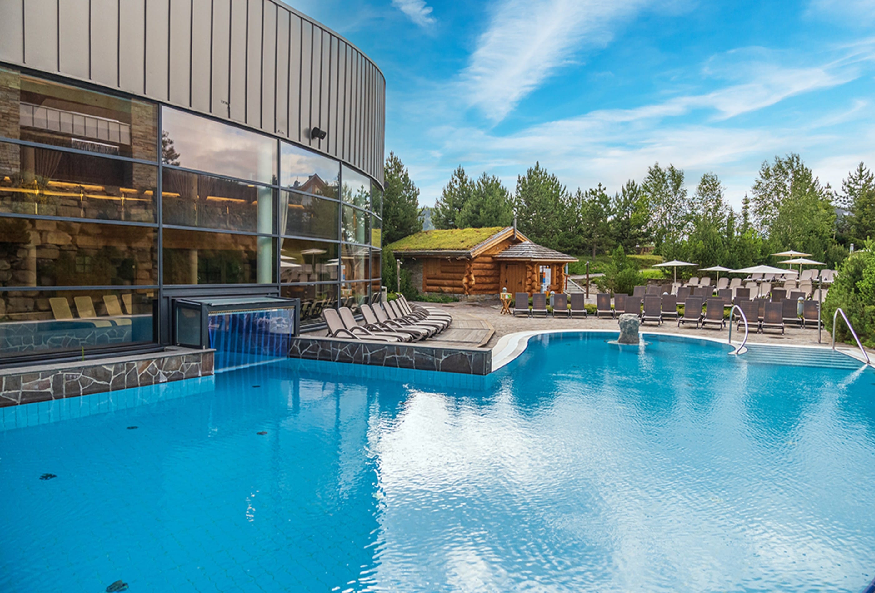 Outdoor thermal pool at Terma Bania with sun loungers and wooden sauna cabin in summer