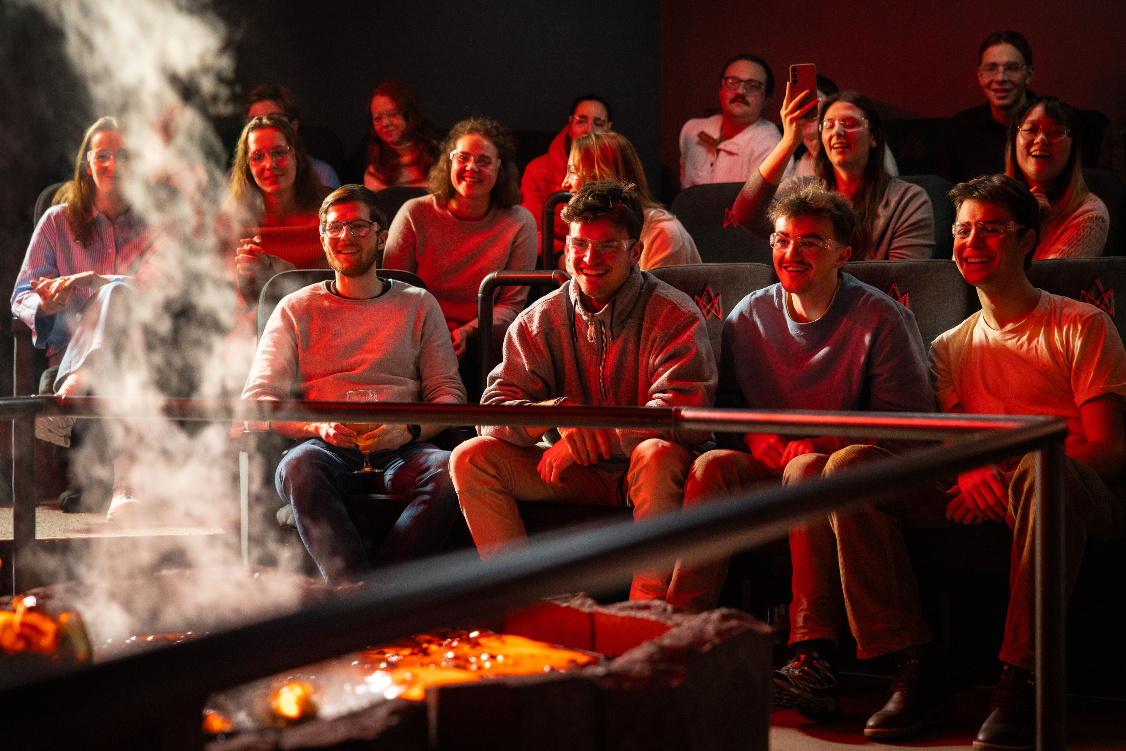 An audience seated in a dark theater watches molten lava being poured into a trench, glowing yellow-orange under stage lights.