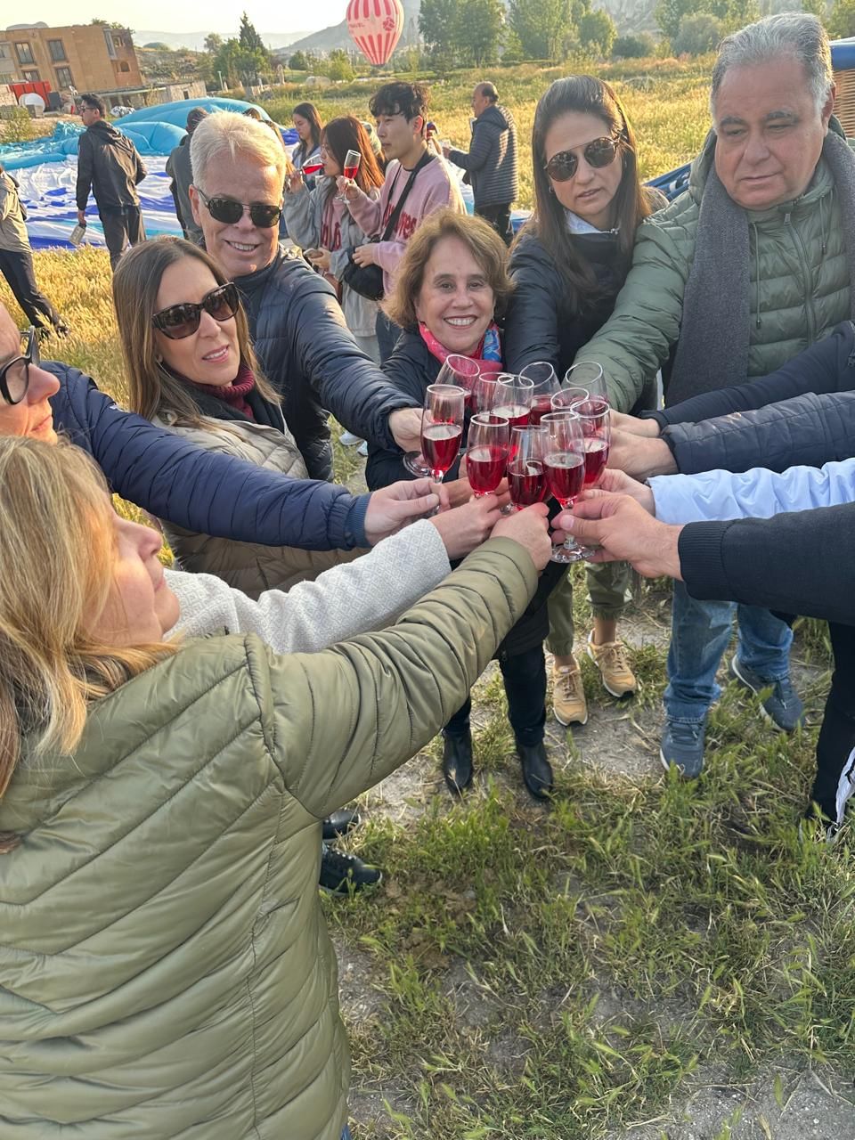 “Tour group raising champagne glasses and smiling happily outdoors, celebrating after a hot air balloon ride over Cappadocia.”