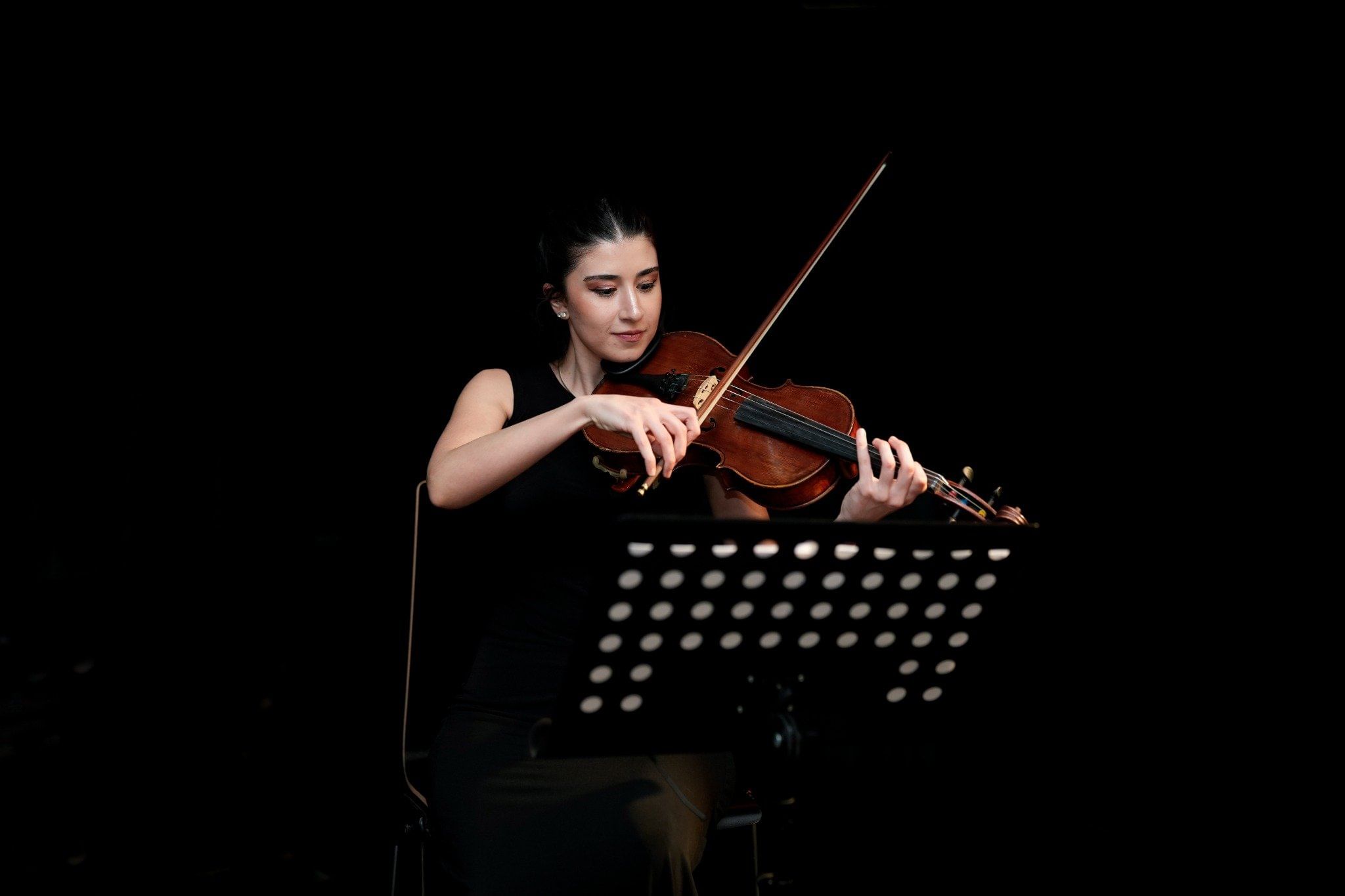 Female violist in black dress playing at Haus der Musik, Vienna, seated behind a music stand.