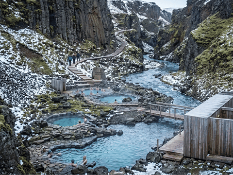 Wide aerial view of Húsafell Canyon Baths showing multiple steaming geothermal pools along a glacial river canyon in winter