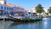 Moliceiro boats on Aveiro canal with colorful waterfront buildings and passengers