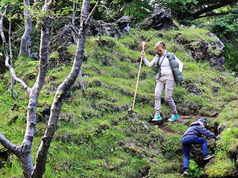 Girl climbing down a hill among rocks and greenery in Hellisgerði