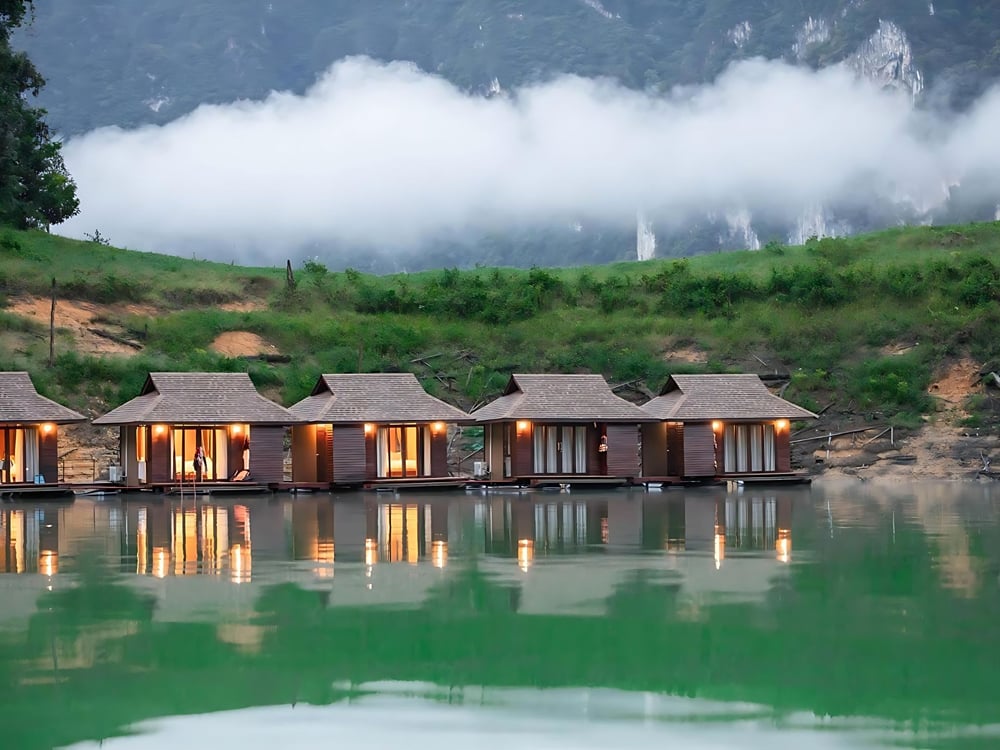 Floating bungalows lit at dusk, reflected in the lake