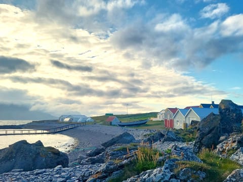 A bay with a floating jetty extending out into it and a number of brightly coloured farm buildings close by.