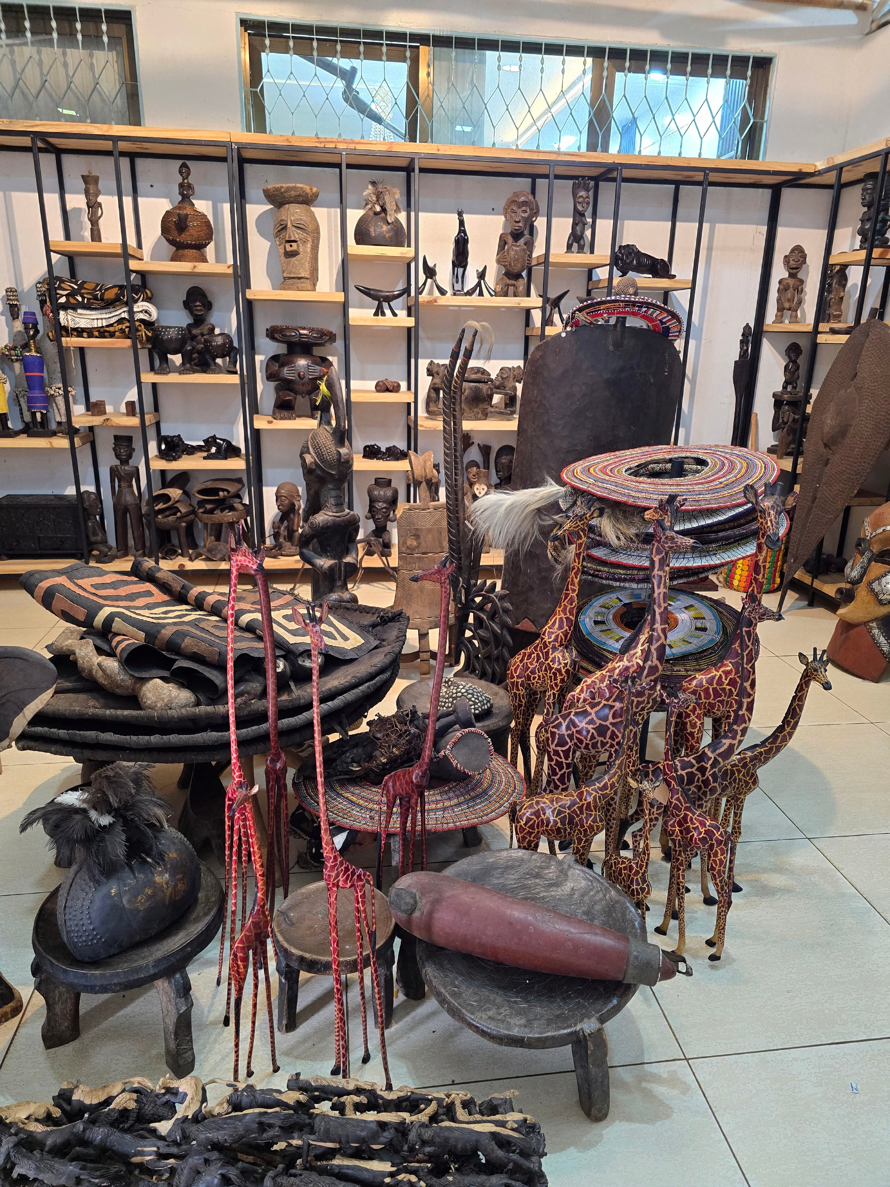 A detailed display of hand-carved African wooden sculptures, decorative masks, and artisanal collectibles inside a gift shop.