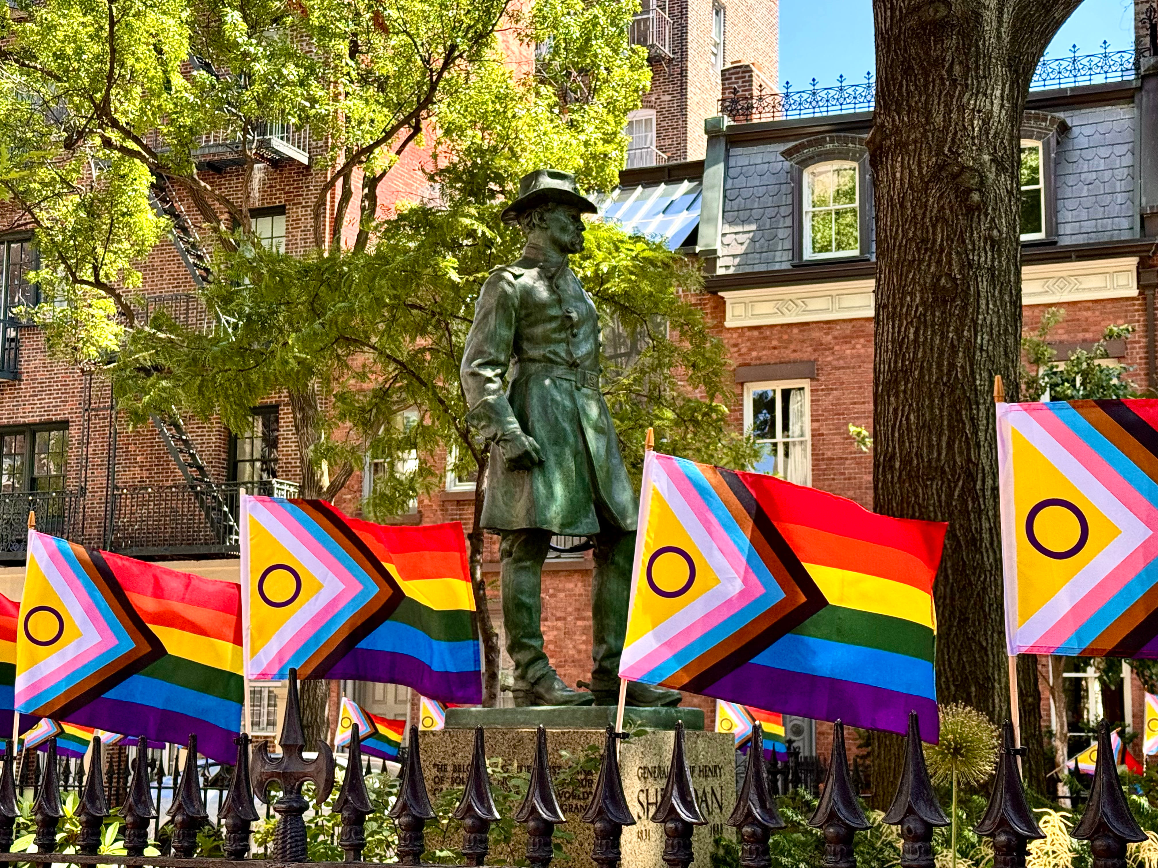 Pride flags line a fence in Christopher Park in front of a statue.