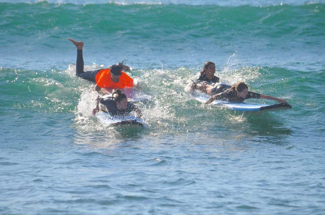 Group surf lesson at Cerritos Beach with students paddling on surfboards in small waves