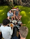 Group of travelers having a picnic lunch on a wooden boat on Lake Duluti surrounded by lush green nature.