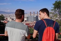 Tourists standing on Montjuic hill watching the panoramic view of Barcelona. Office building with three chimneys in the background.