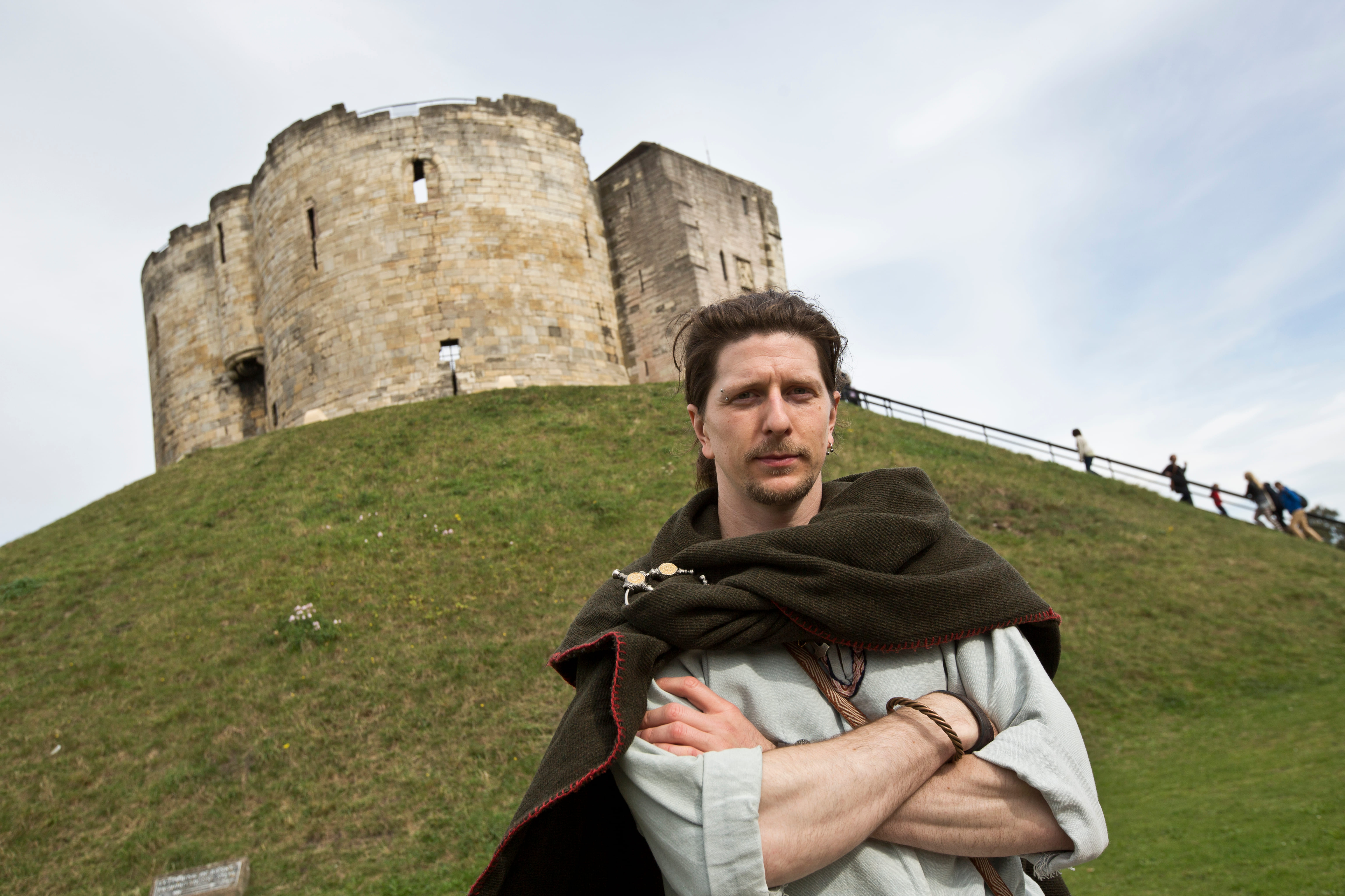 A viking-costumed tour guide standing with arms folded in front of Clifford's Tower, a Norman Keep, in York.