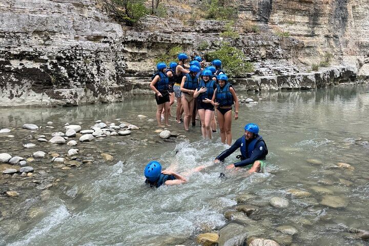 A group of people swimming and enjoying themselves in a clear river with a guide leading the fun , surrounded by natural greenery .