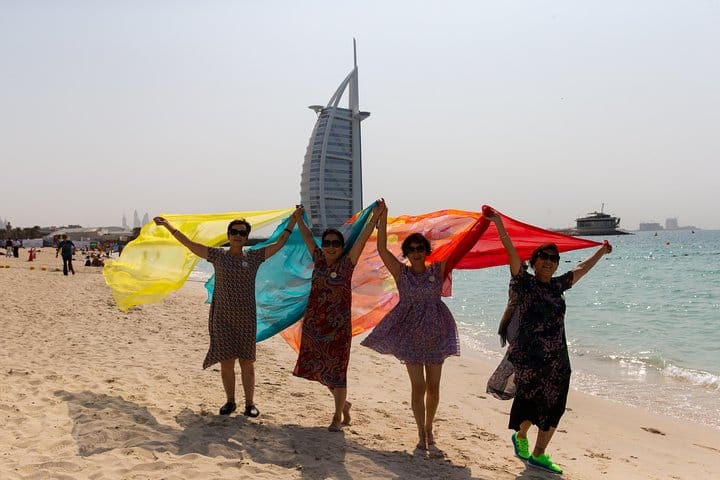 Travelers take pictures on the beach in front of the Burj al Arab hotel.