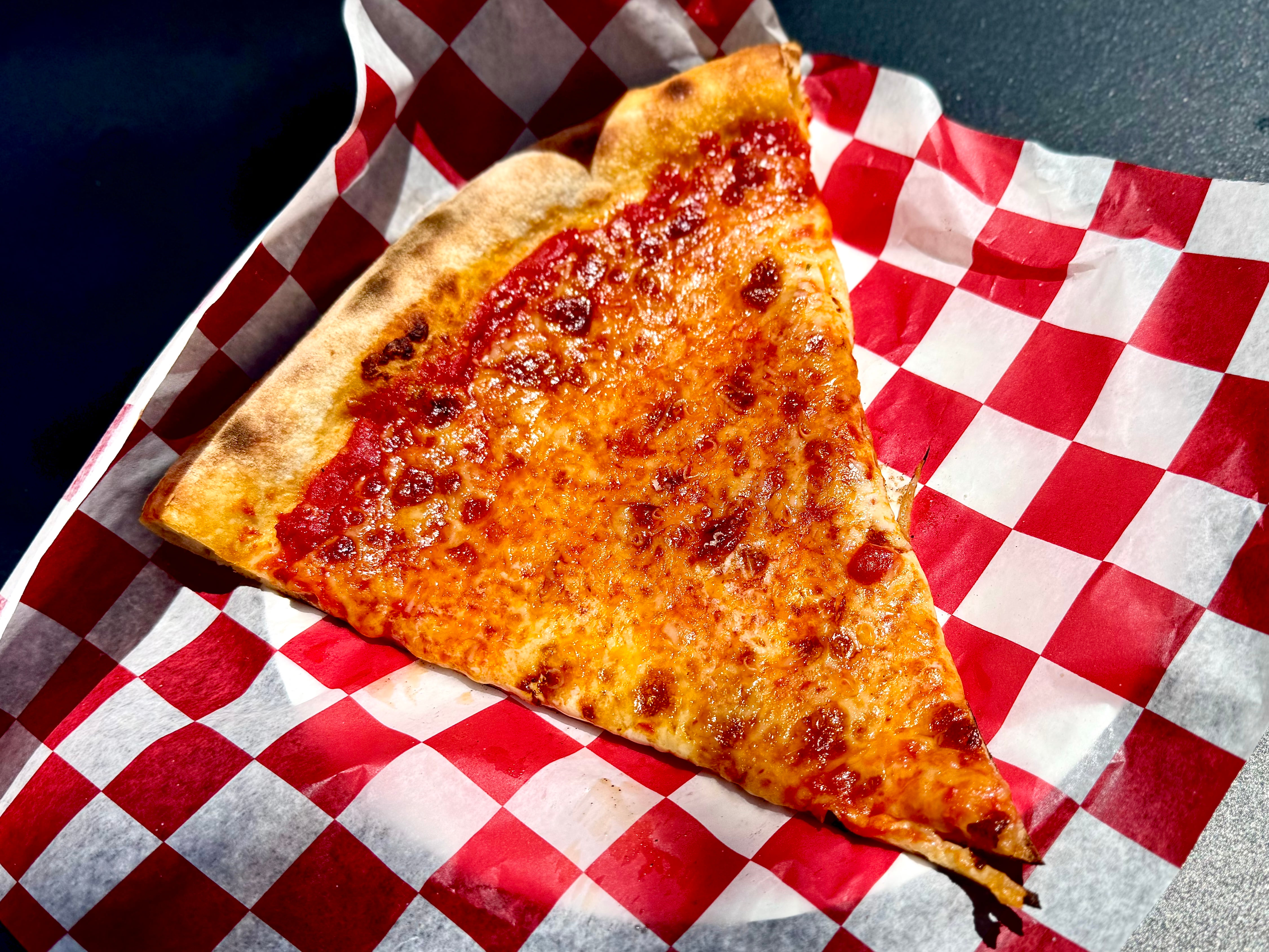 A classic cheese pizza slice served on red-and-white checkered paper.