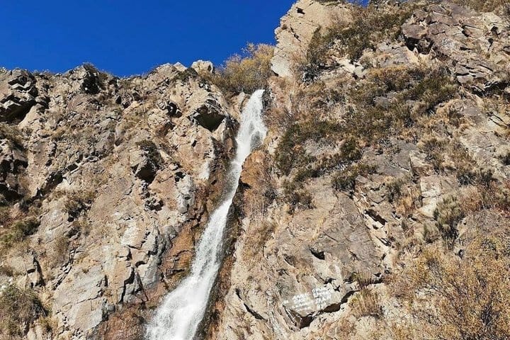 Powerful waterfall flowing through rocky cliffs and pine forest in Turgen Gorge, Kazakhstan.