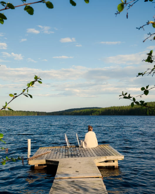A person sitting by the lakeside, relaxing after a traditional Finnish sauna experience at StayLapland in Rovaniemi.
