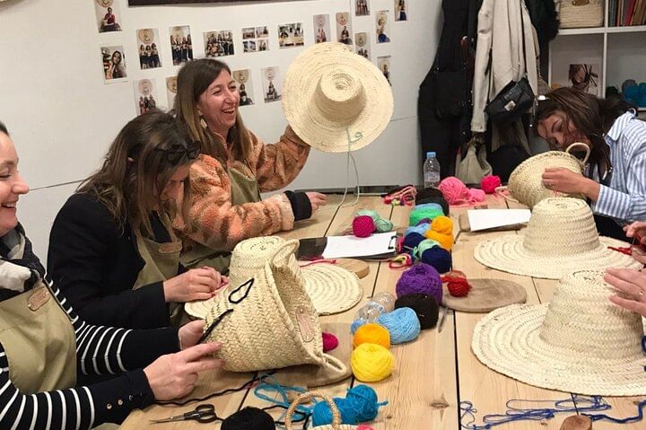 Participants sitting around a large table, embroidering their straw hats with colorful threads during the workshop.