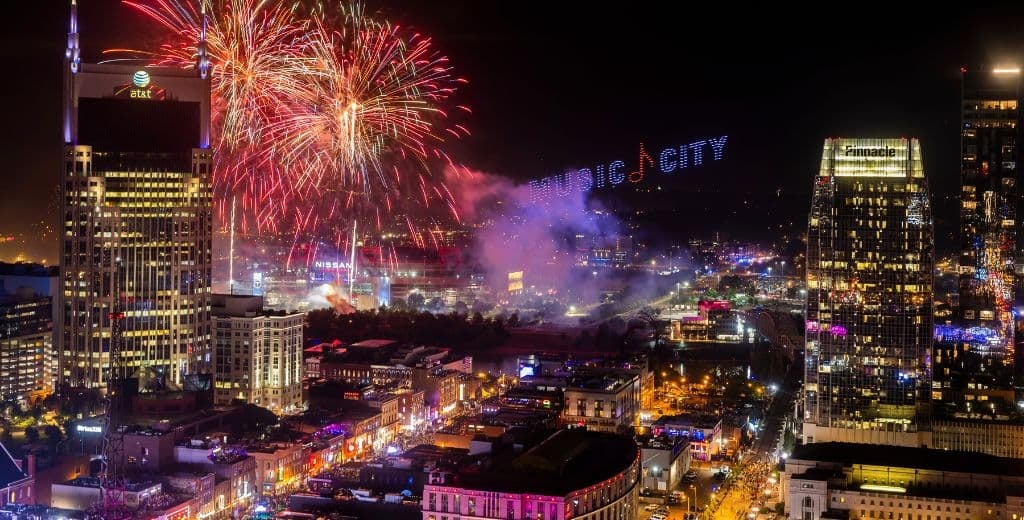 Nashville skyline at night with fireworks over Broadway and a “Music City” light display illuminating the downtown streets.