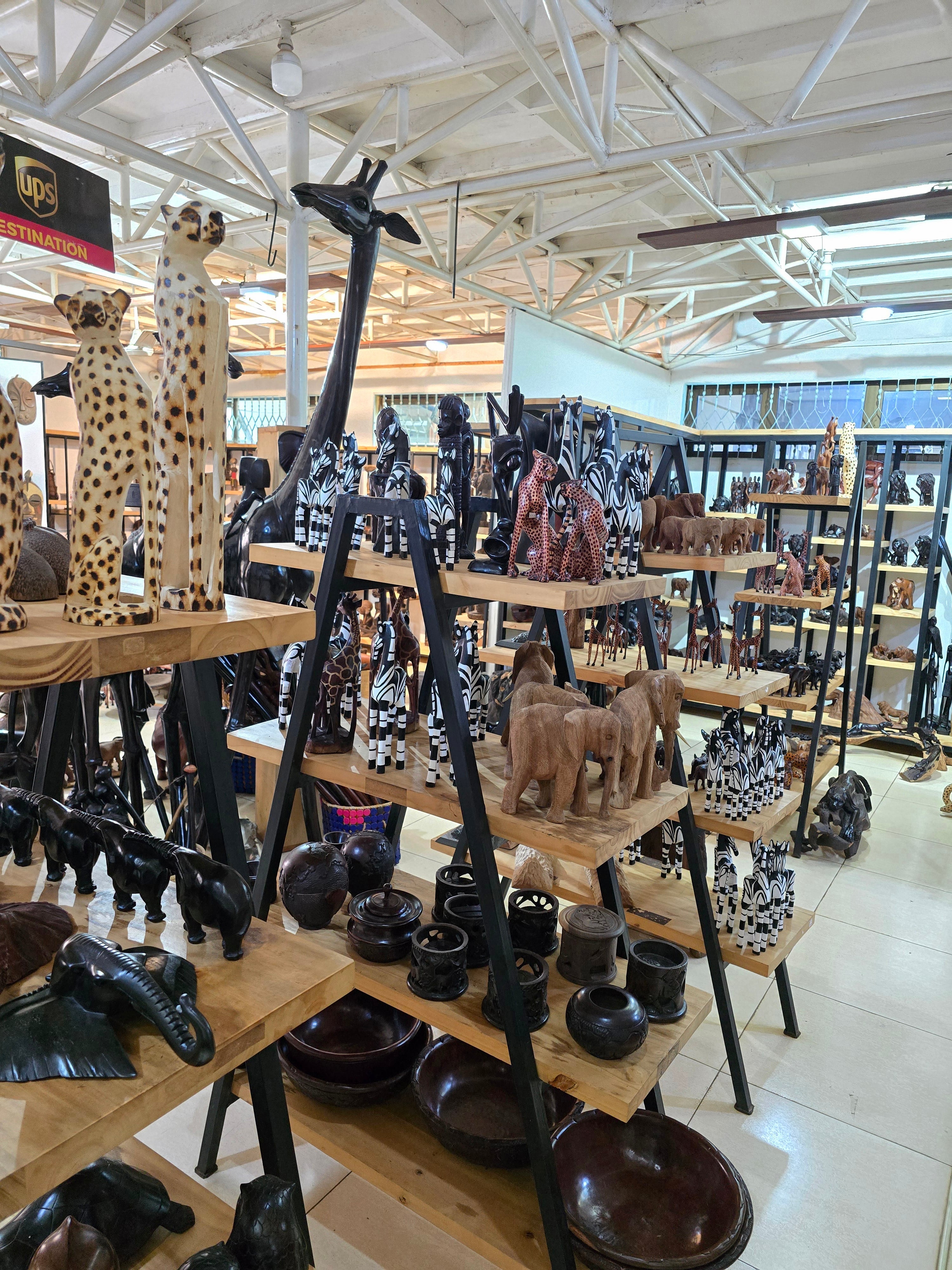 Wooden shelves displaying finely carved animal figurines, statues, and traditional African art pieces in a souvenir shop.