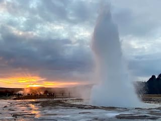 The geyser Strokkur erupting  in the winter, with a low Sun in the background