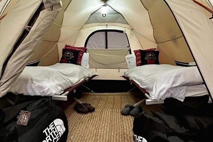 Interior view of a high-altitude camping tent featuring two elevated cots with white bedding and pillows.