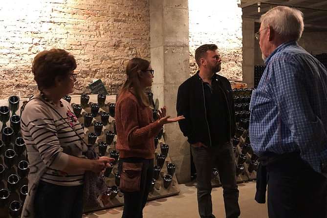 A lady explains how to make Cava in the basement of the cava maker. In the background you see Champagne bottles stored in racks.