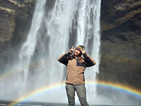 A woman staning in front of a waterfall and a rainbow