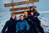 Four hikers smiling in front of the Uhuru Peak sign at the summit of Mount Kilimanjaro in Tanzania.