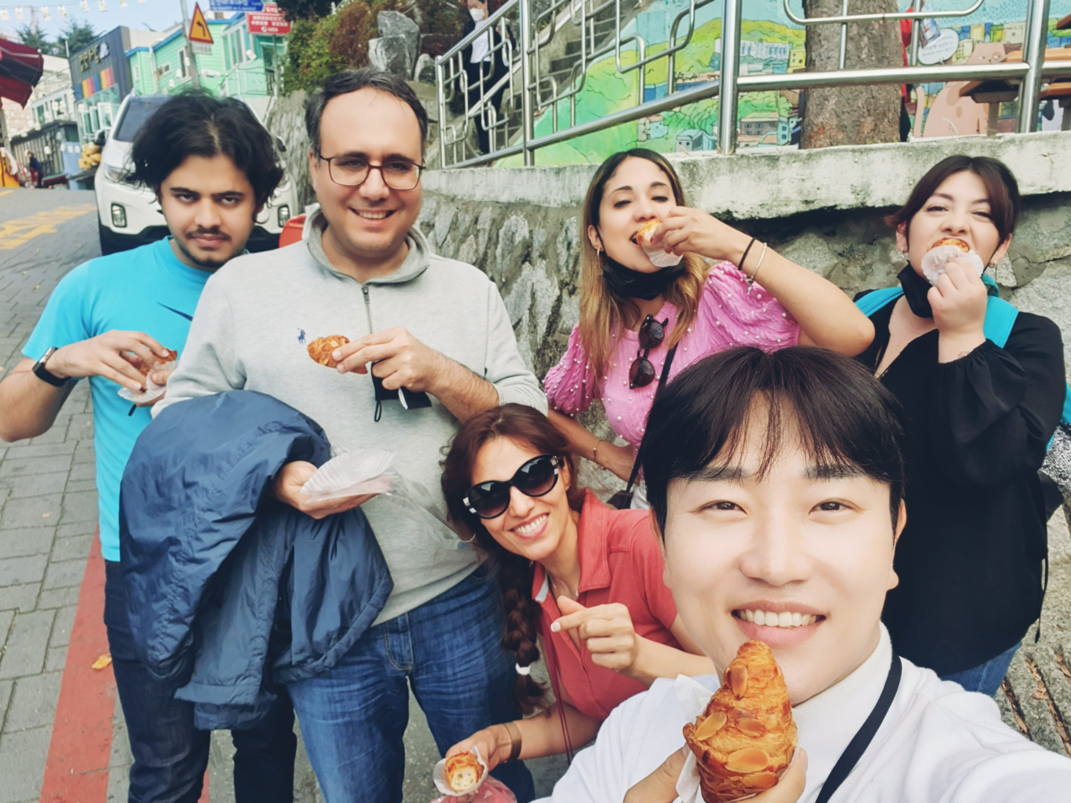Group of travelers smiling and eating Korean sweet pancakes (hotteok) together at Gamcheon Culture Village in Busan