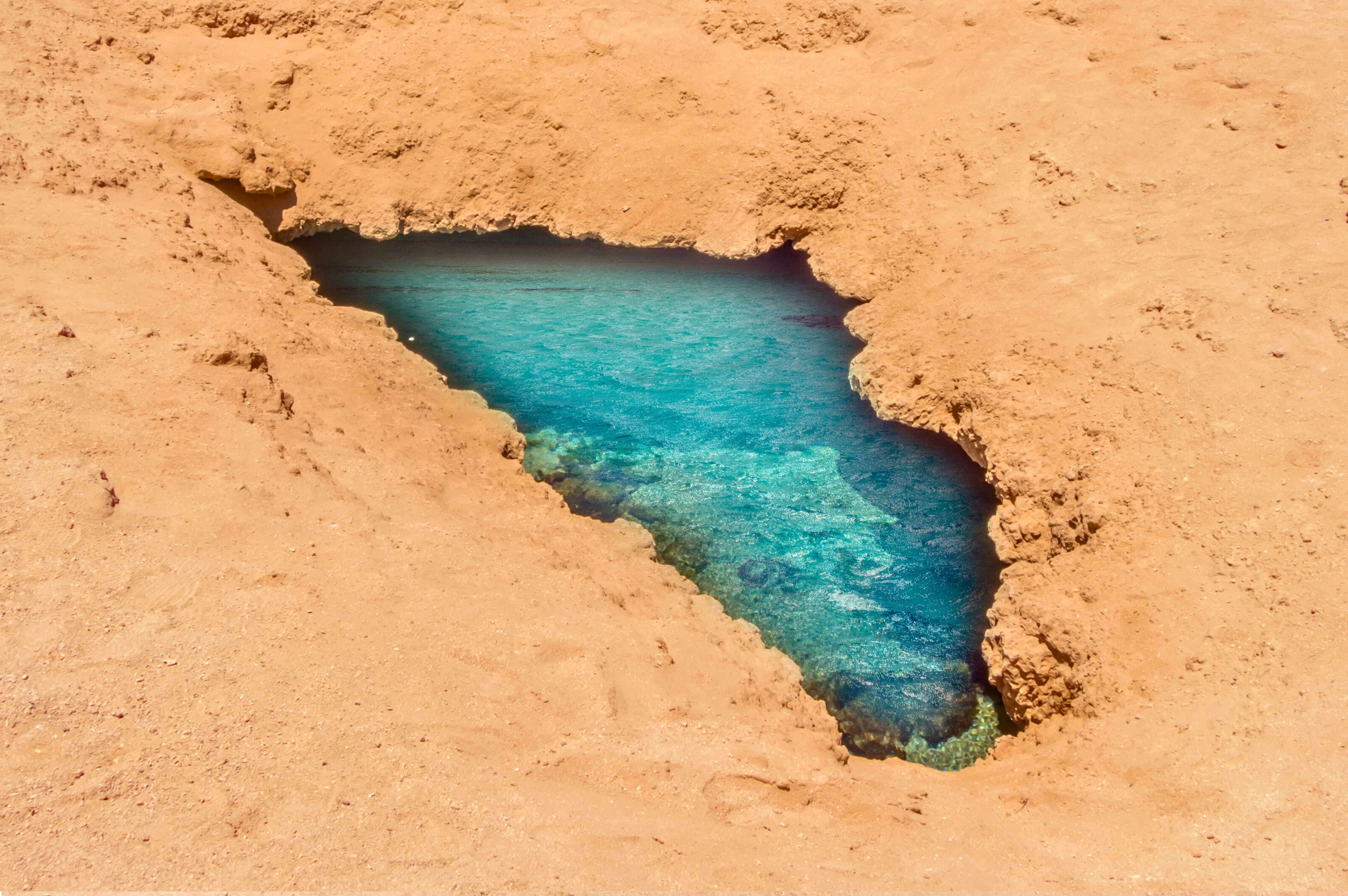 Bright turquoise natural pool of water nestled within the textured, warm orange desert rocks in Ras Mohammed.