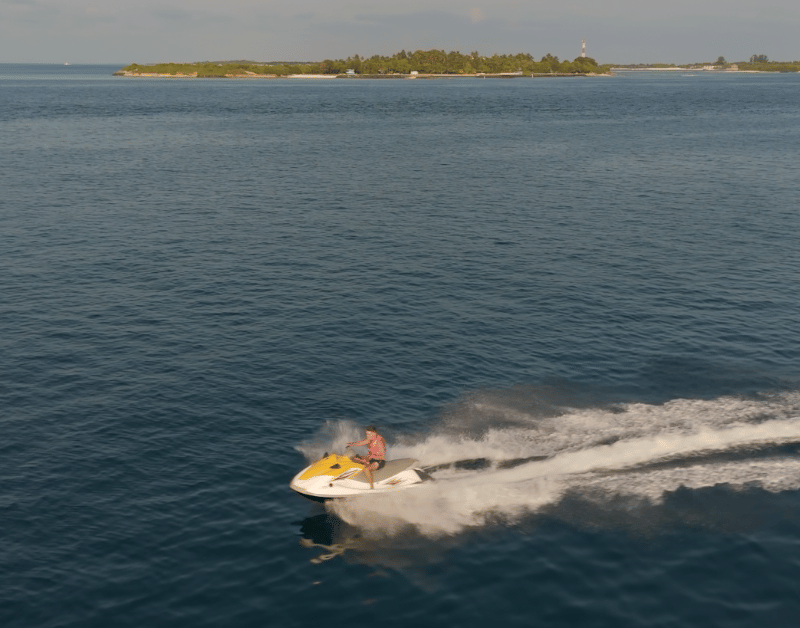 A man riding a jet ski in front of Himmafushi Island, with turquoise waters and tropical scenery in the background