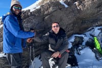 A climber and a guide in winter gear smiling together against a rocky, snow-covered mountain backdrop.