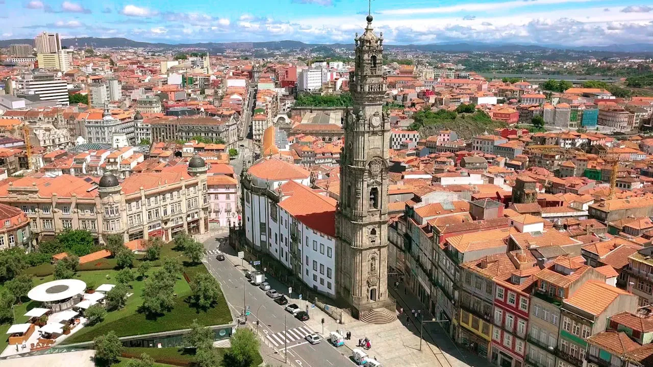 An aerial view shows a tall, ornate stone tower rising above a dense urban landscape of orange-tiled roofs at Clérigos Tower & Museum Ticket.