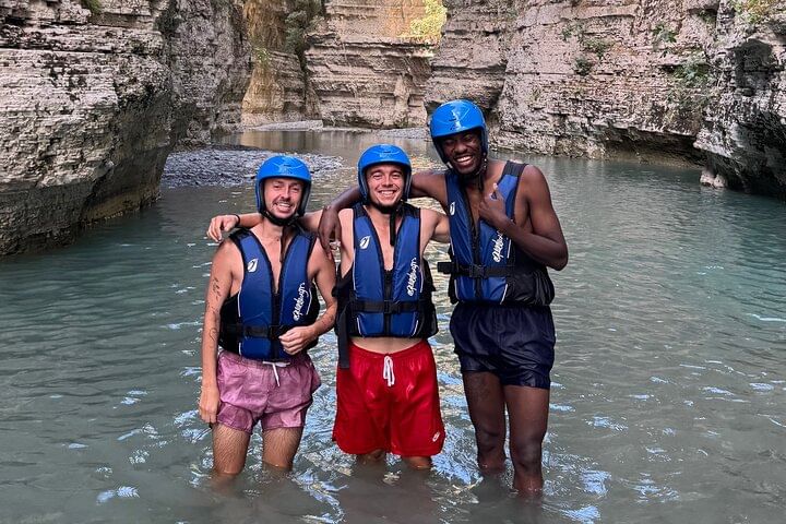 Group of people exploring the canyon , walking through water and rocks , enjoying the experience together .