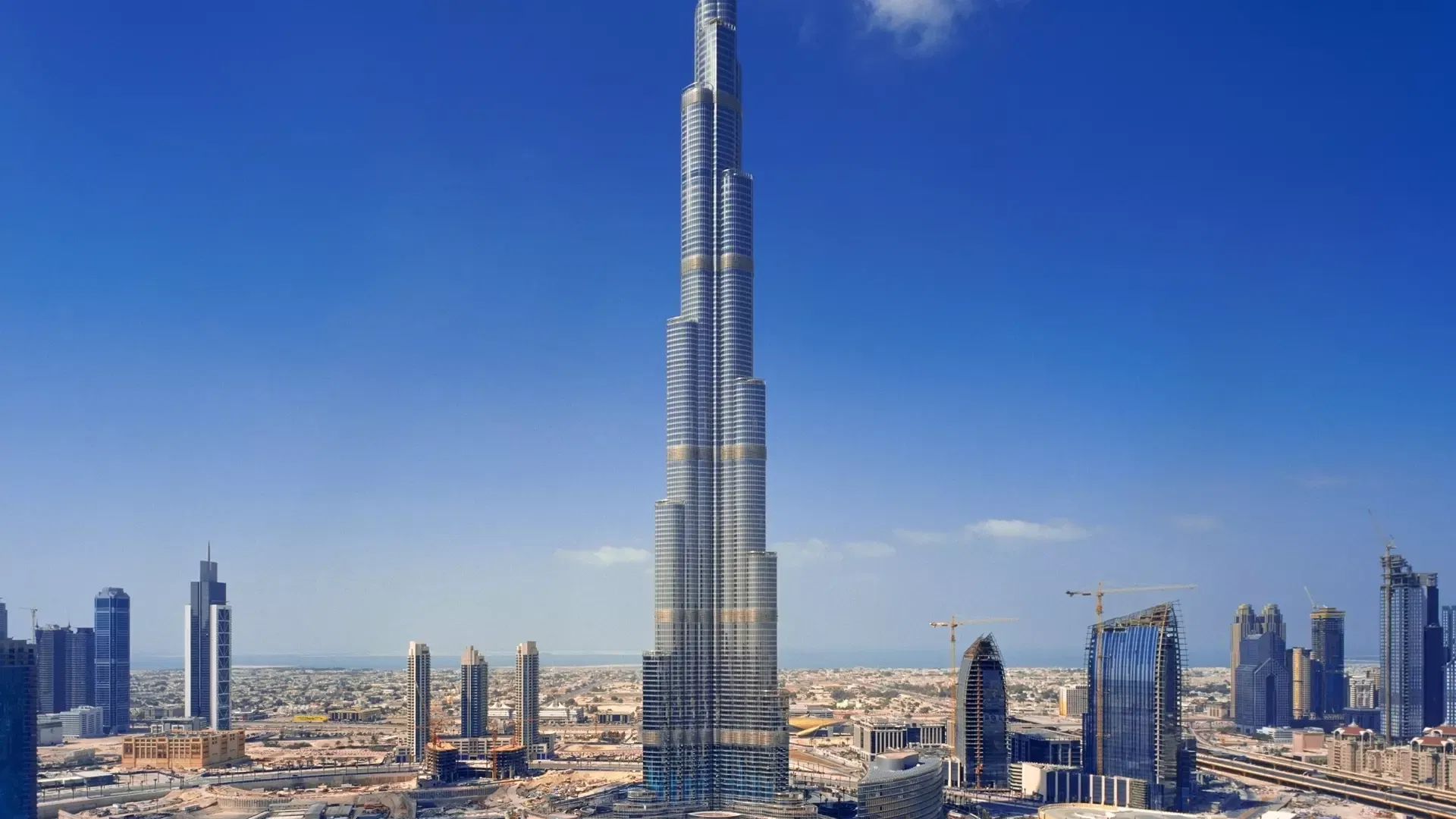 The tower seen in full from a distance by day, dwarfing the surrounding Downtown skyline under a clear blue sky at Burj Khalifa