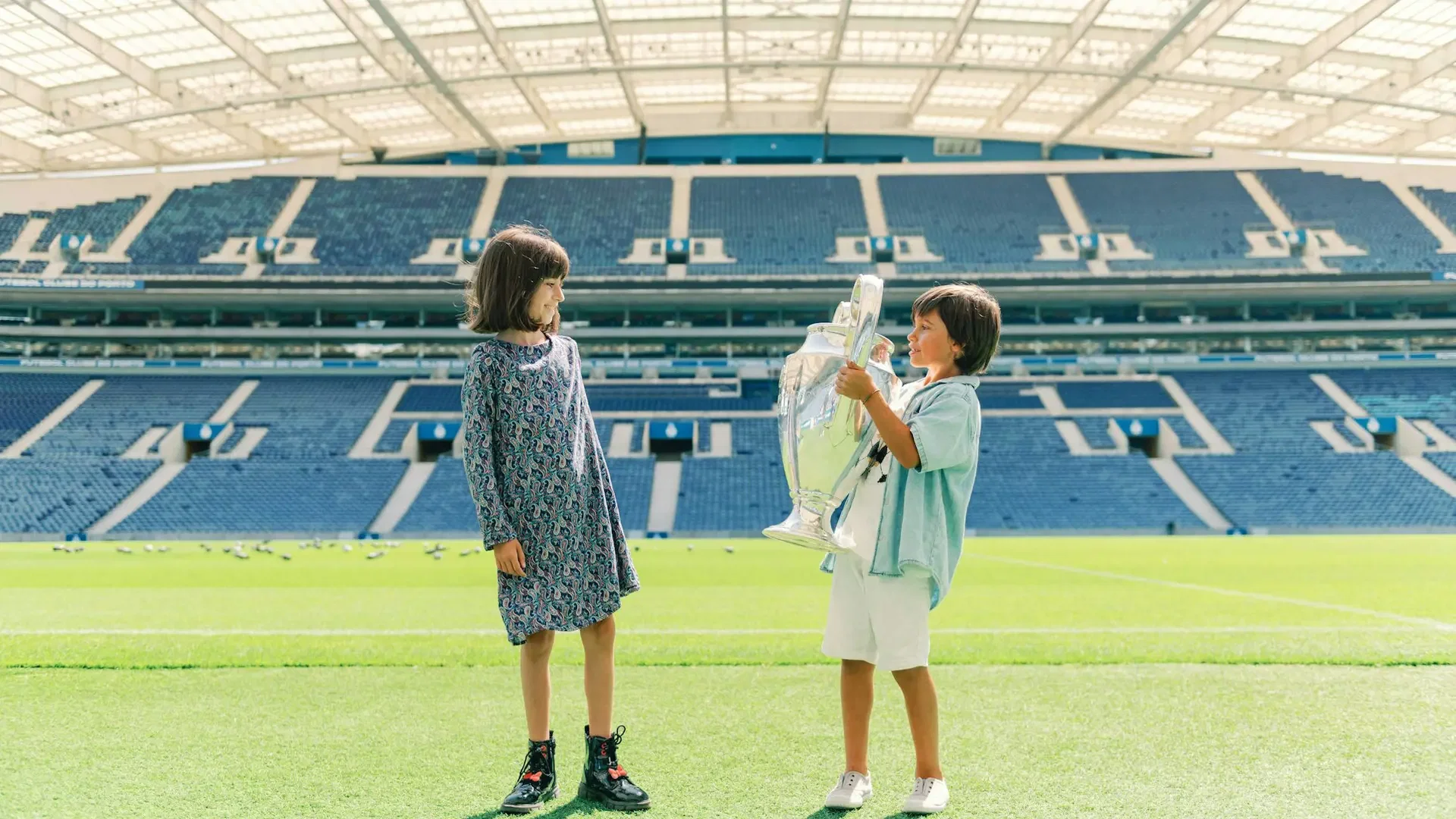 Two children stand on a stadium pitch holding a large silver trophy at FC Porto Museum & Dragão Stadium ticket.