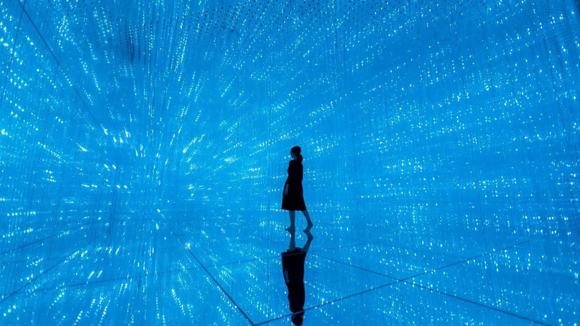 A single visitor in dark clothing stands in an immersive digital room filled with vertical strands of glowing blue lights at COMBO: Tokyo Skytree + teamLab Planets TOKYO Tickets.