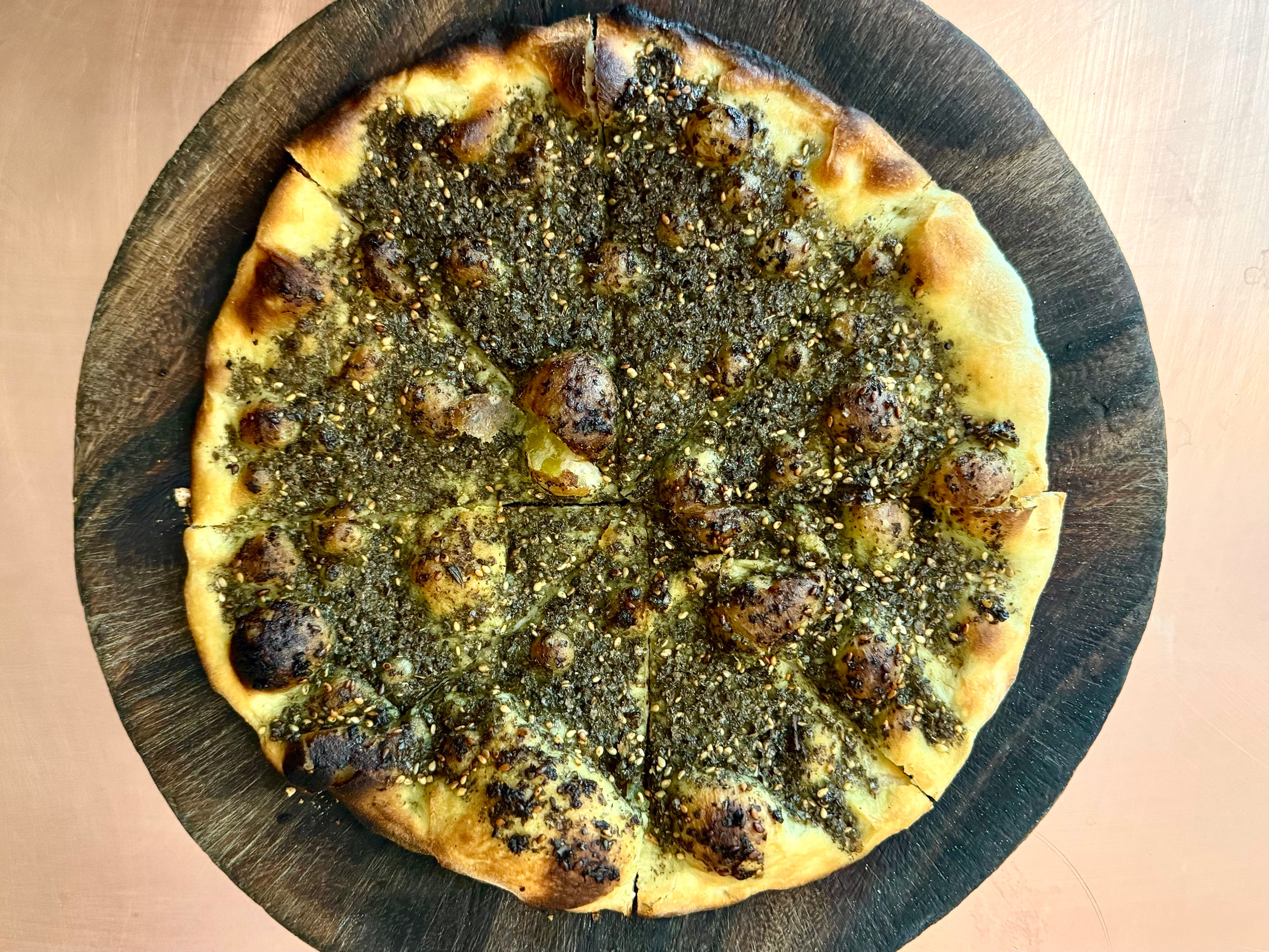A round za’atar flatbread on a wooden plate atop a copper counter.