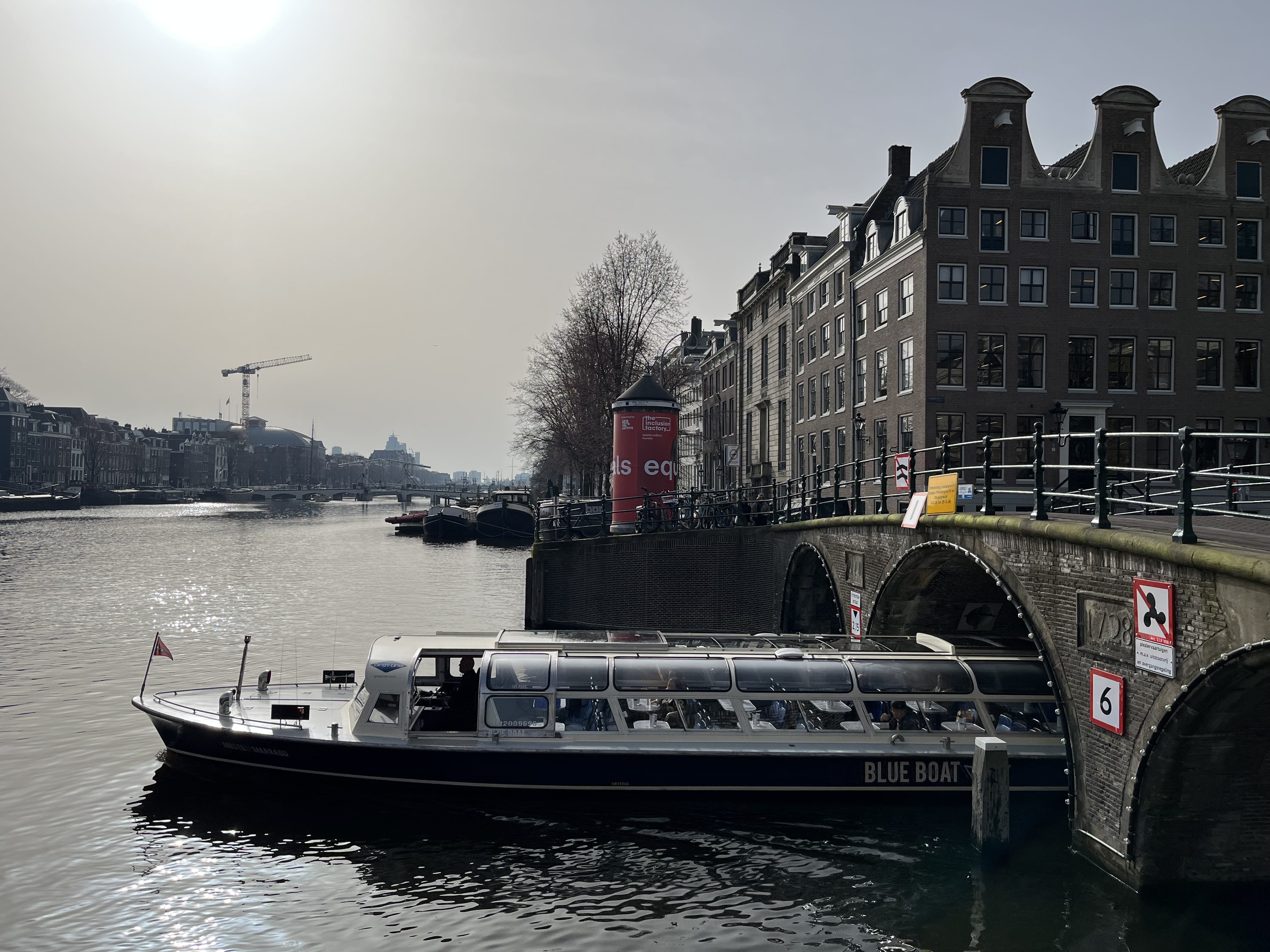 Amsterdam canal cruise boat near historic bridge with passengers enjoying city views