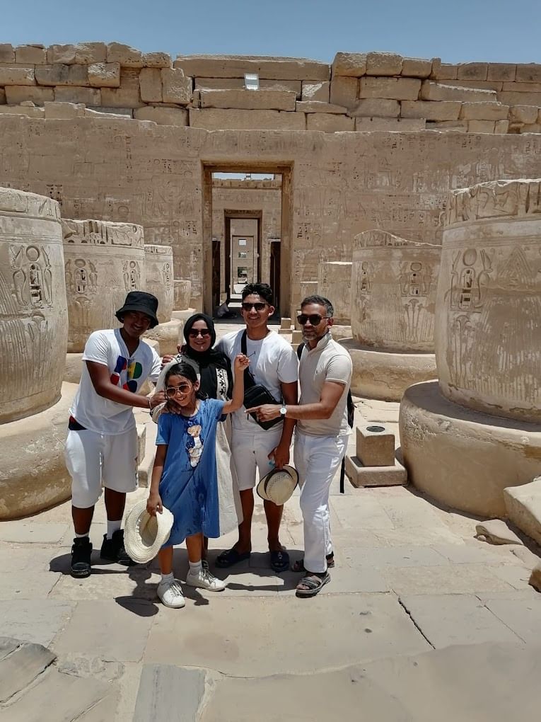 Un groupe de cinq personnes posant et souriant parmi d'anciennes colonnes de pierre ornées de hiéroglyphes sur le site d'un temple historique à Louxor, en Égypte.