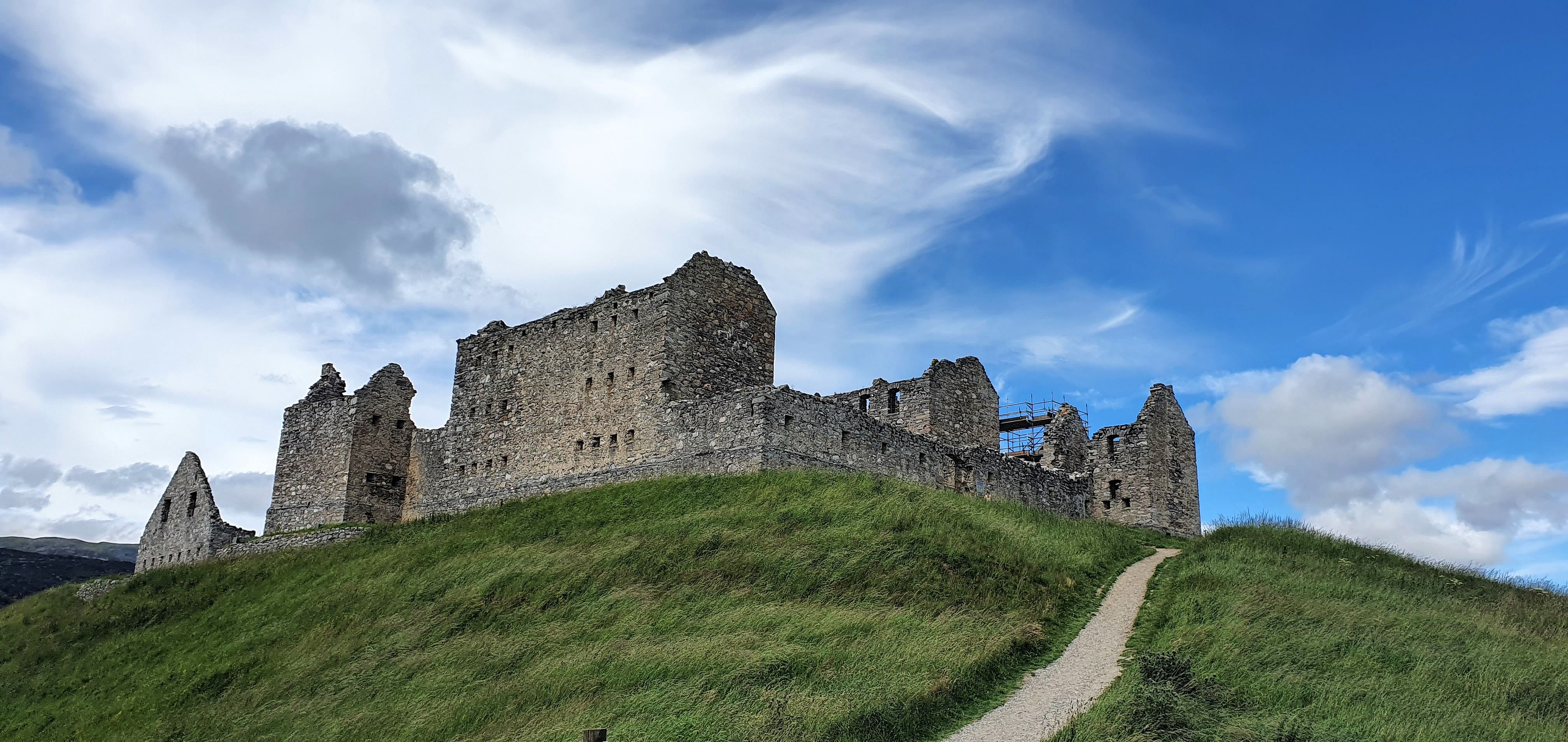 An 18th Century historical Scottish castle ruin set high on a grassy mound. the background has a summer sky; blue with high clouds.