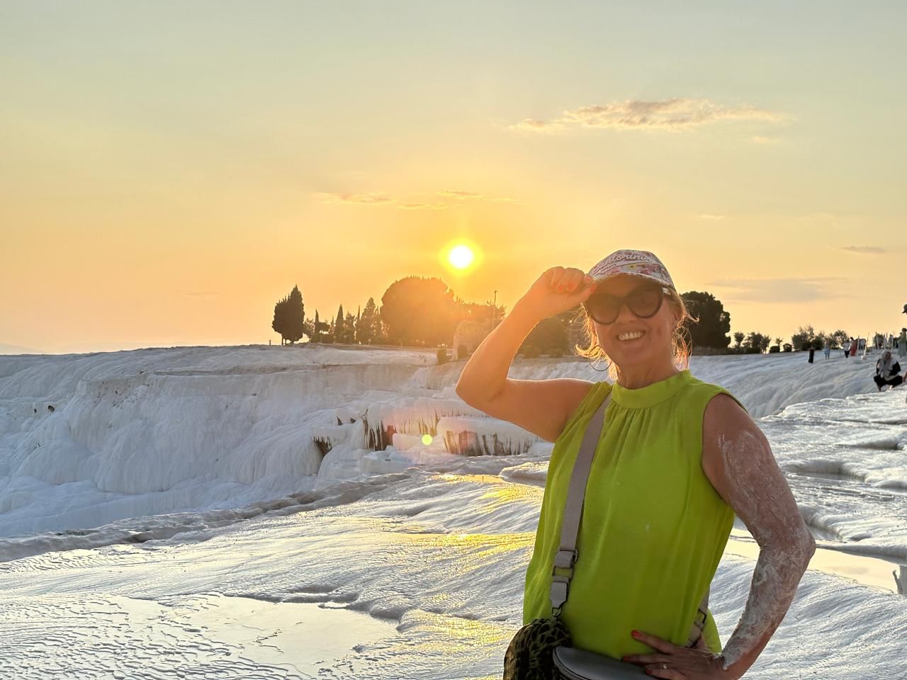 “Our tour guide smiling and posing at Pamukkale’s white terraces during a vibrant sunset with warm orange and pink hues.”