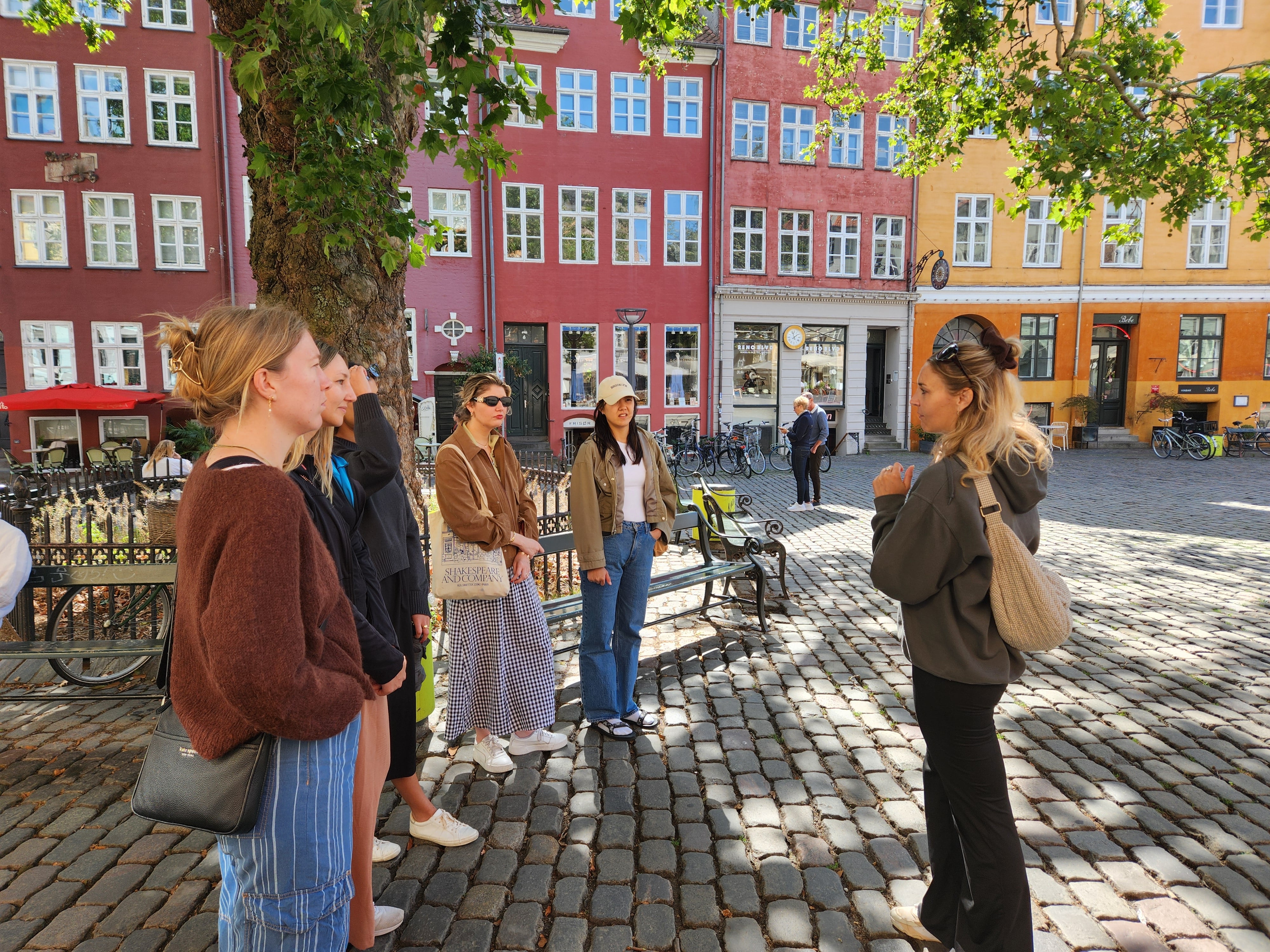 A local guide talks with a group of visitors on a cobblestone square surrounded by colorful historic buildings in Copenhagen.